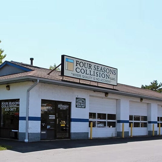 A white building with a brown roof and a sign reading Four Seasons Collision