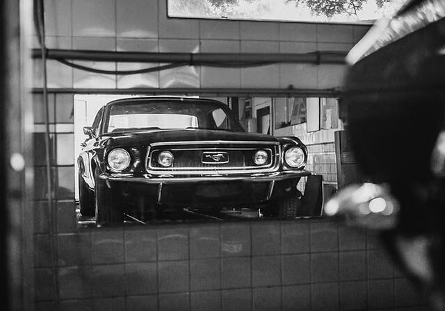 A classic Ford car parked in a garage. The car's reflection is visible in a shiny surface.