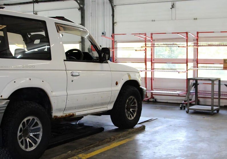 A white SUV parked on a lift in a garage. The vehicle is positioned for maintenance or repair.
